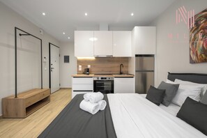A modern hotel room with a bed, a small kitchenette, a wooden bench, and a large painting on the wall. - Terra Suites, Nilie Hospitality MGMT (Thessaloniki)