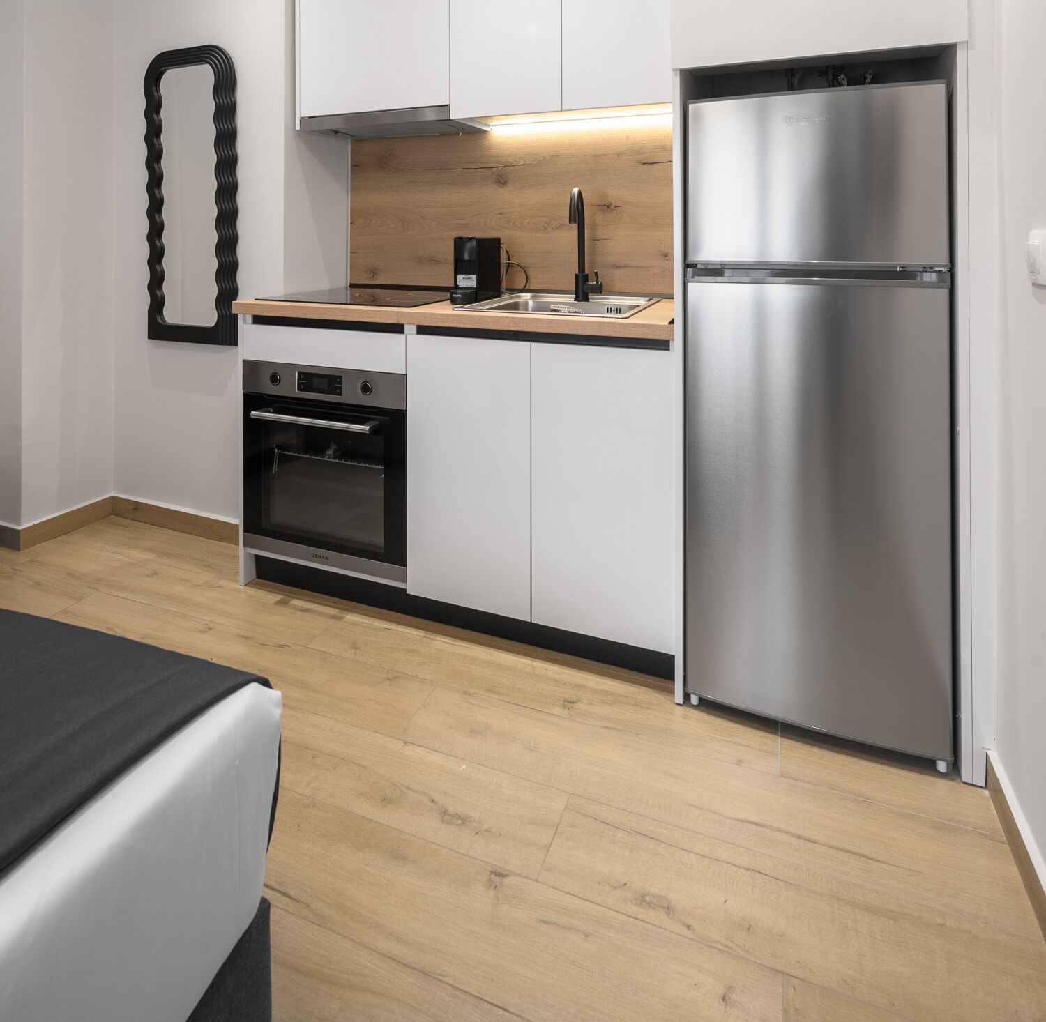 Une cuisine moderne avec des armoires blanches, un réfrigérateur en acier inoxydable, un four encastré et un plan de travail en bois.