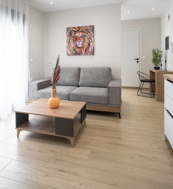 A modern living room with a grey sofa, a wooden coffee table, and a vibrant abstract painting on the wall. - Terra Suites, Nilie Hospitality MGMT (Thessaloniki)