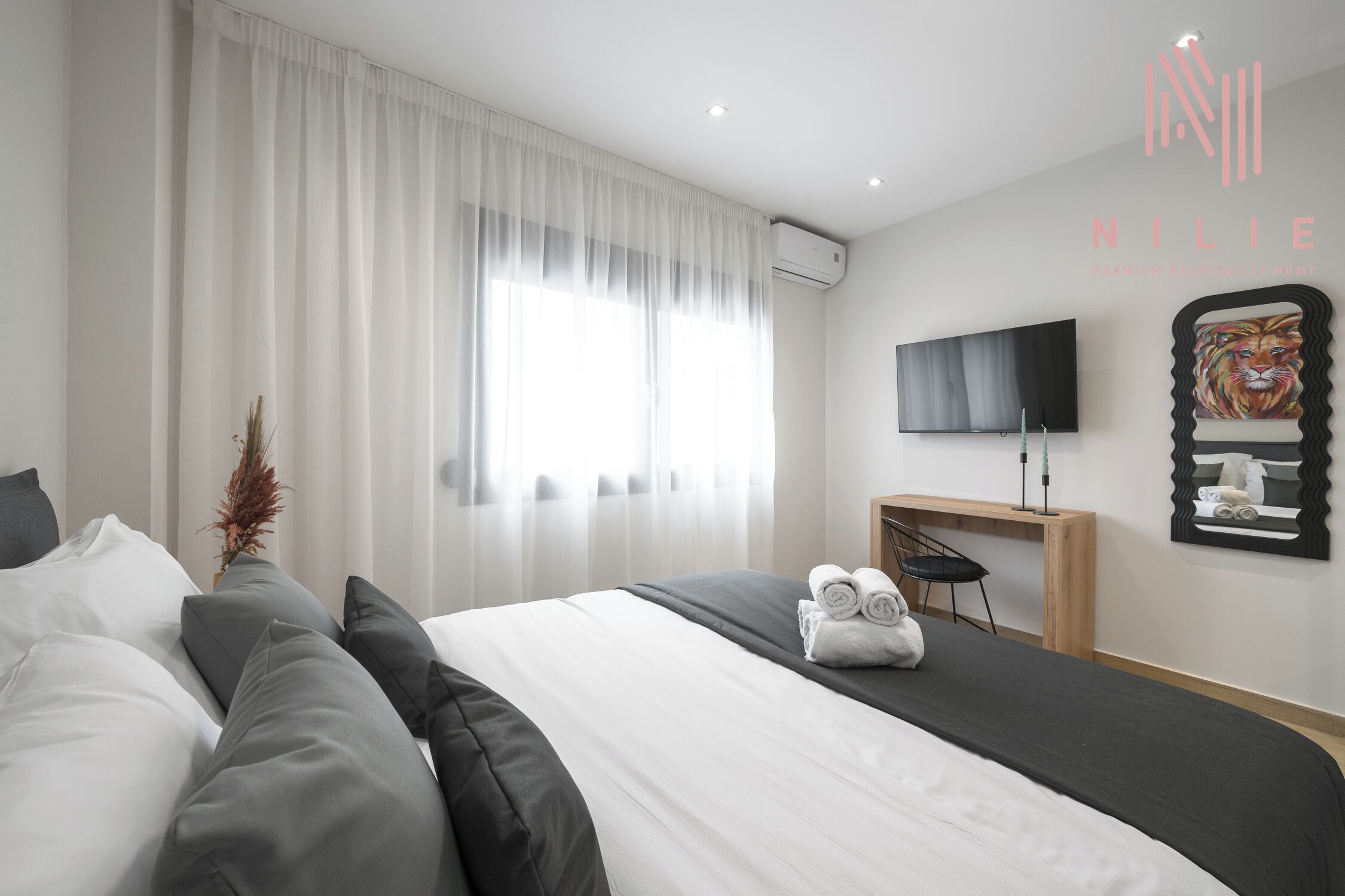 Une chambre d’hôtel moderne avec un lit bien fait, un téléviseur à écran plat fixé au mur et un miroir décoratif orné d’une tête de tigre.