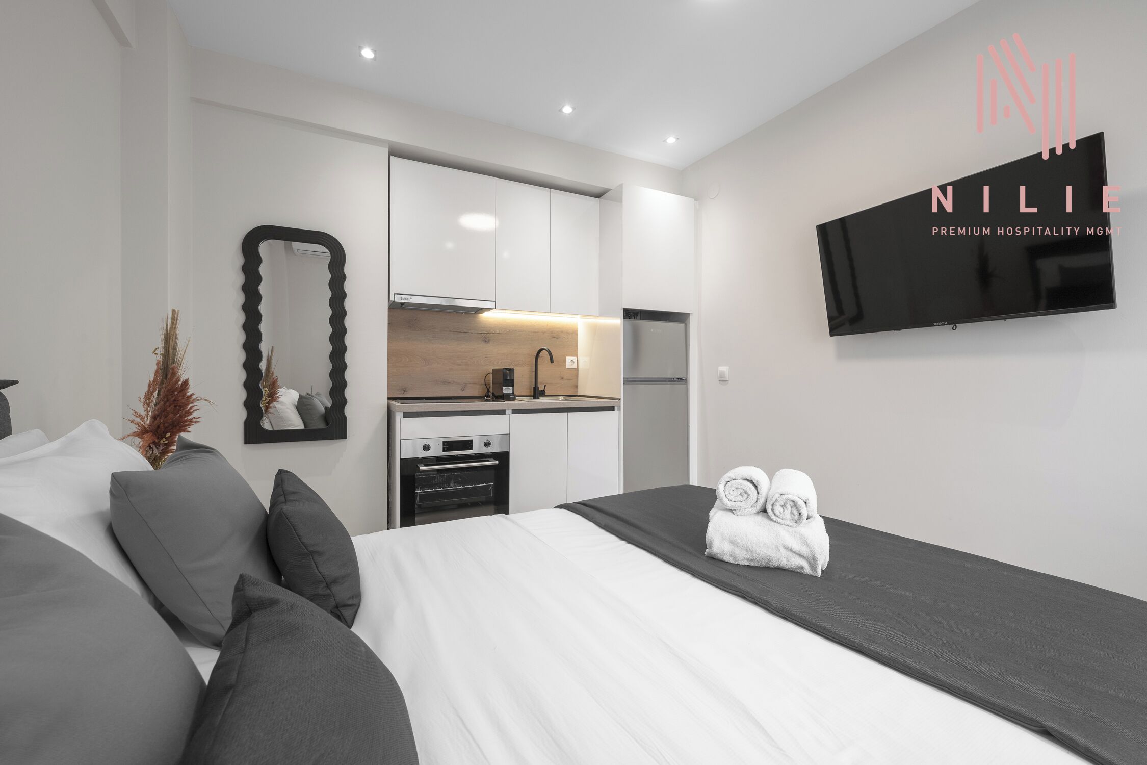 Une chambre d’hôtel moderne dotée d’un grand lit, d’une télévision à écran plat, d’une kitchenette et d’un miroir.