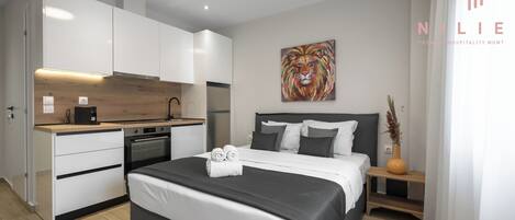 A modern hotel room with a bed, a small kitchenette, and a painting on the wall.