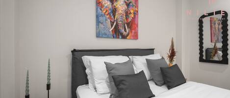 A modern bedroom with a large bed, a colorful elephant painting, and a black mirror on the wall.