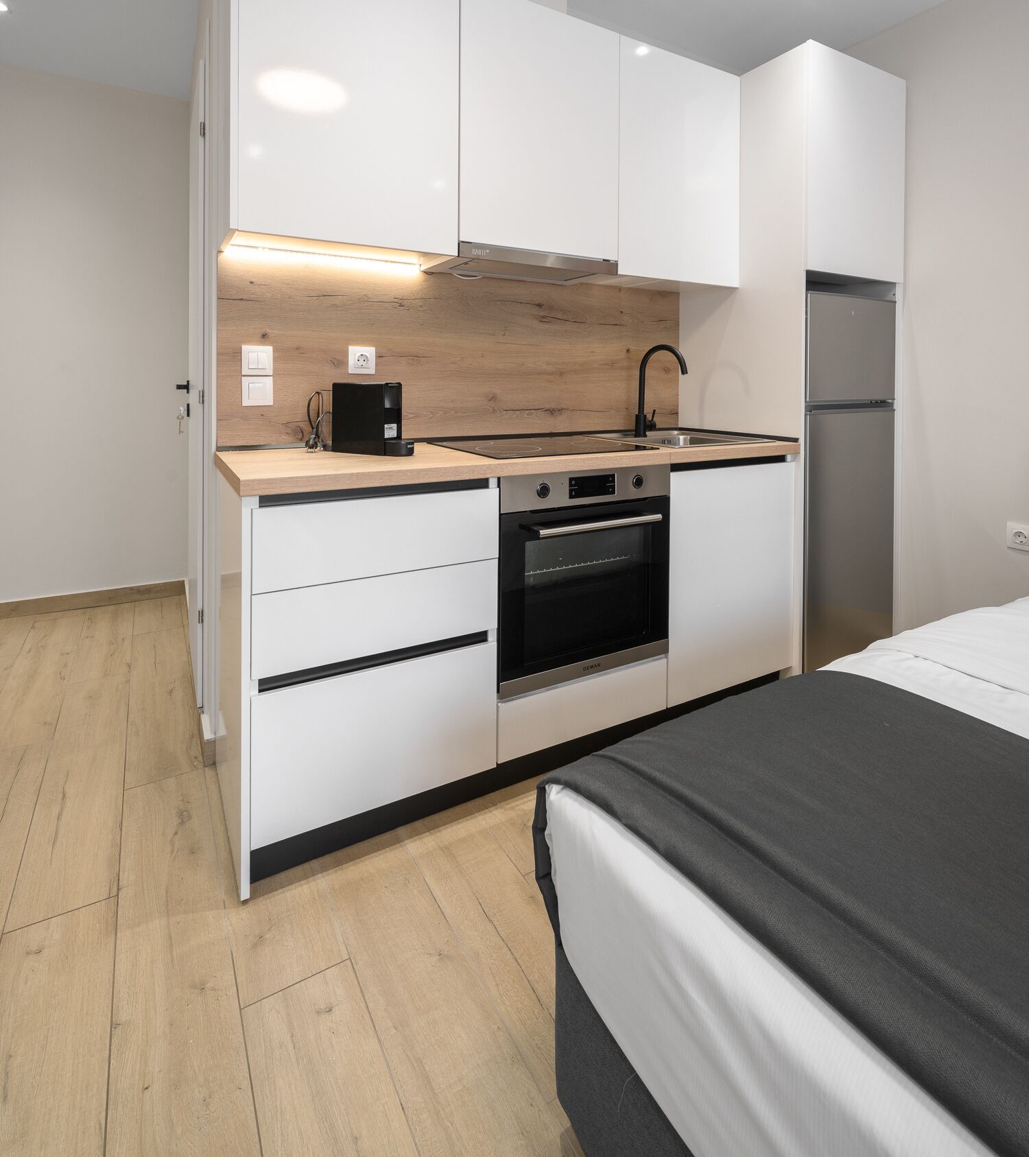 A compact kitchen with a built-in oven, a coffee machine, and a refrigerator.