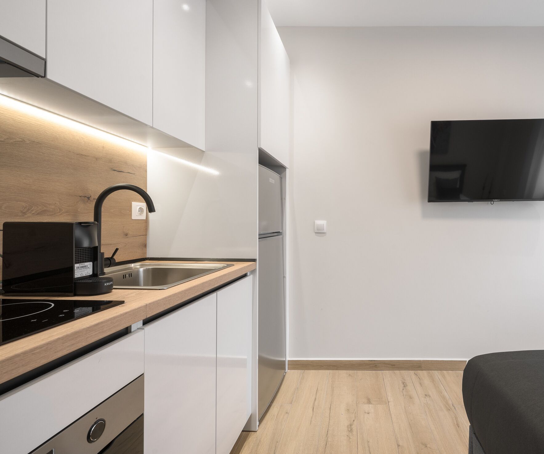 A modern kitchen with a built-in stove, sink, and a flat-screen TV mounted on the wall.