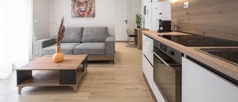 A modern kitchen with a wooden countertop and built-in oven, a grey sofa with cushions, and a vase with dried plants.