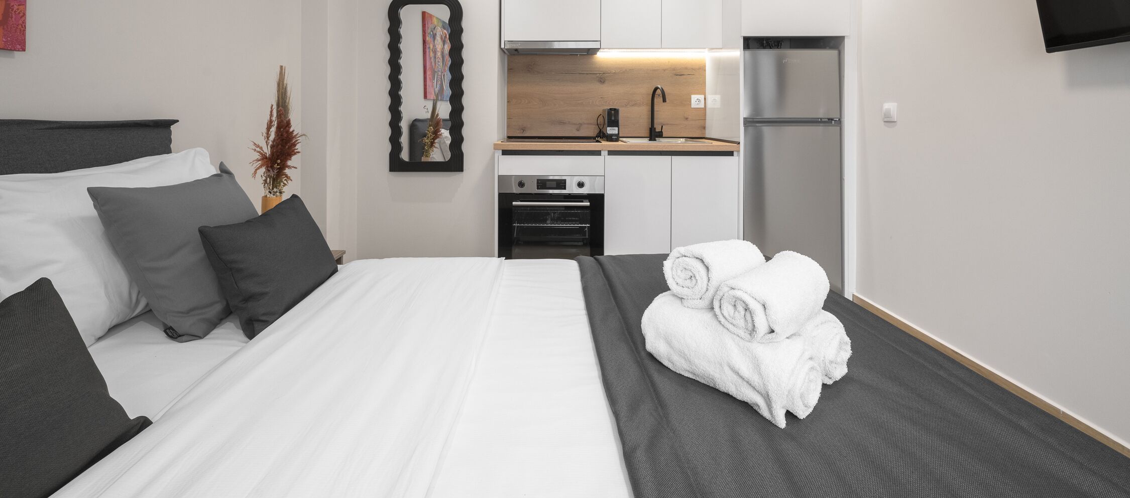 A hotel room with a bed, a small kitchenette, a refrigerator, and a mirror.