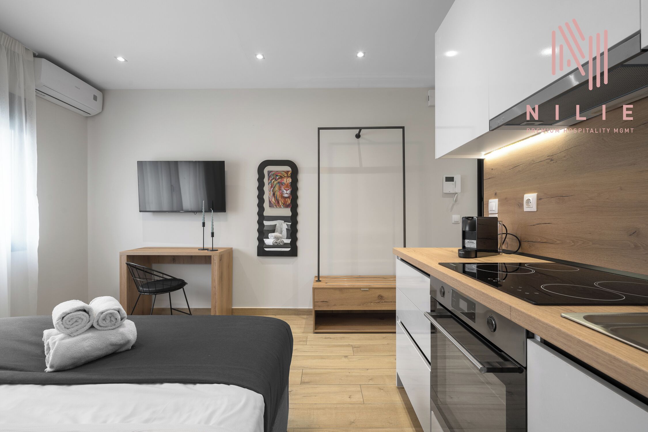 Een moderne hotelkamer met een bed, een bureau, een televisie, een kitchenette met fornuis, en kunst aan de muur.