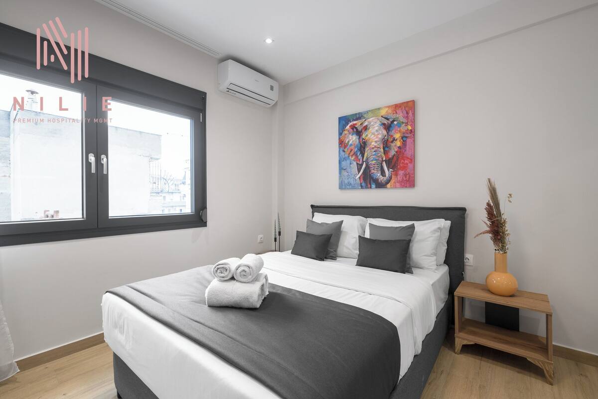 A modern hotel room with a large bed, a window, and a colorful elephant painting on the wall.