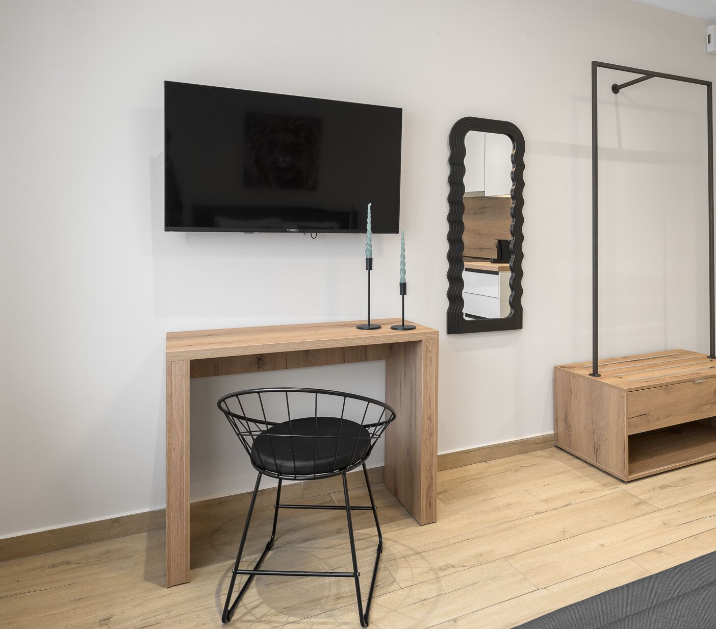Ein modernes Zimmer mit einem Holztisch, einem schwarzen Drahtstuhl, einem an der Wand montierten Fernseher, einem dekorativen Spiegel und einer Holzbank.