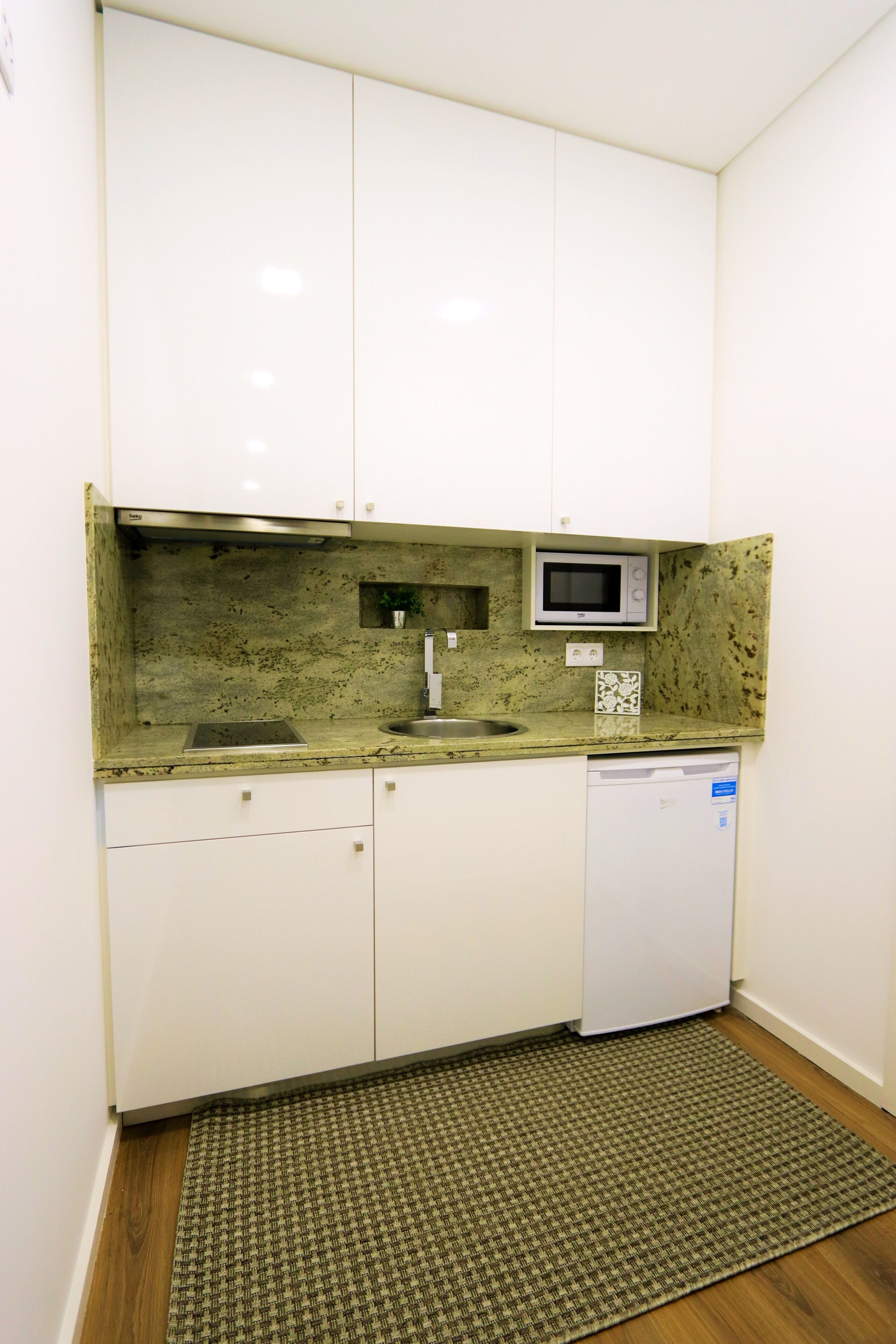 Een kleine keuken met witte kastjes, een magnetron, een spoelbak en een vaatwasser.