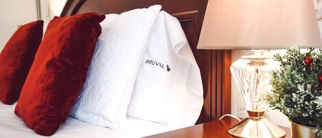 A neatly made bed with a white towel and a red pillow, a bedside lamp, and a small potted plant.
