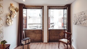 Una habitación con piso de madera, una silla de madera, una mesita con una planta y un adorno en la pared.