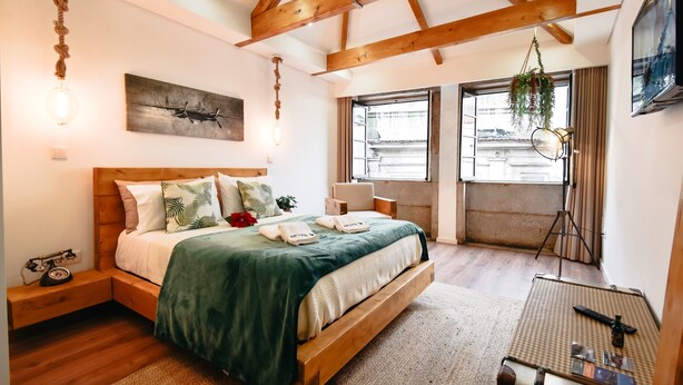 Un dormitorio con una cama de madera, una lámpara colgante, un cuadro y una ventana con cortinas.