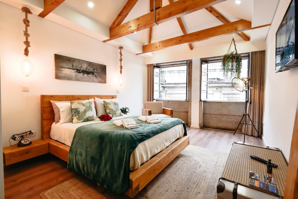 Une chambre à coucher avec un lit en bois, un luminaire suspendu, un tableau et une fenêtre avec des rideaux.
