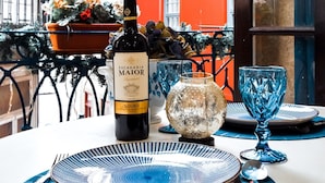 Una mesa dispuesta con una botella de vino Escadia Maior, vasos azules y un florero decorativo.