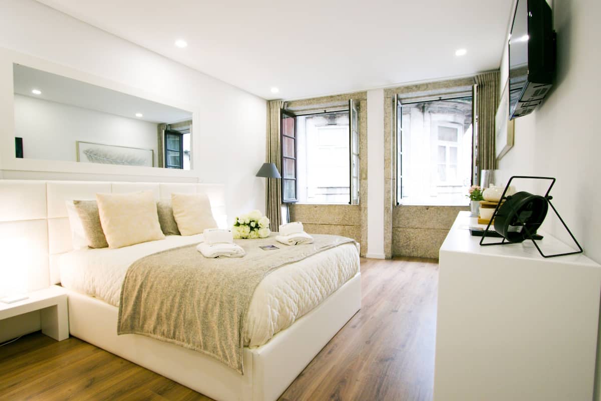 Une chambre moderne avec un grand lit, une table de chevet, un téléviseur à écran plat fixé au mur et une fenêtre avec des rideaux.