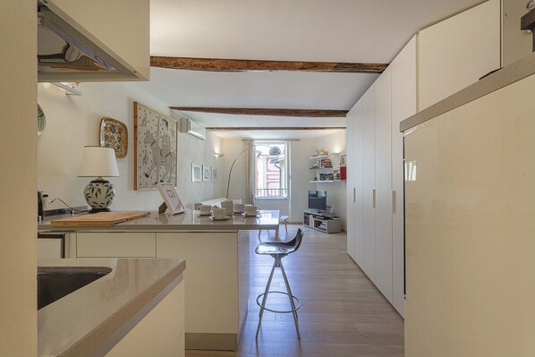 A narrow kitchen with a central island, wooden beams on the ceiling, and a view of the outside through a window.