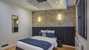 A modern bedroom with a skylight, a large bed with a blue and white duvet, and a textured wall with two wall-mounted lights. - Superb & New Apartment Saint Germain des Pres (Paris)