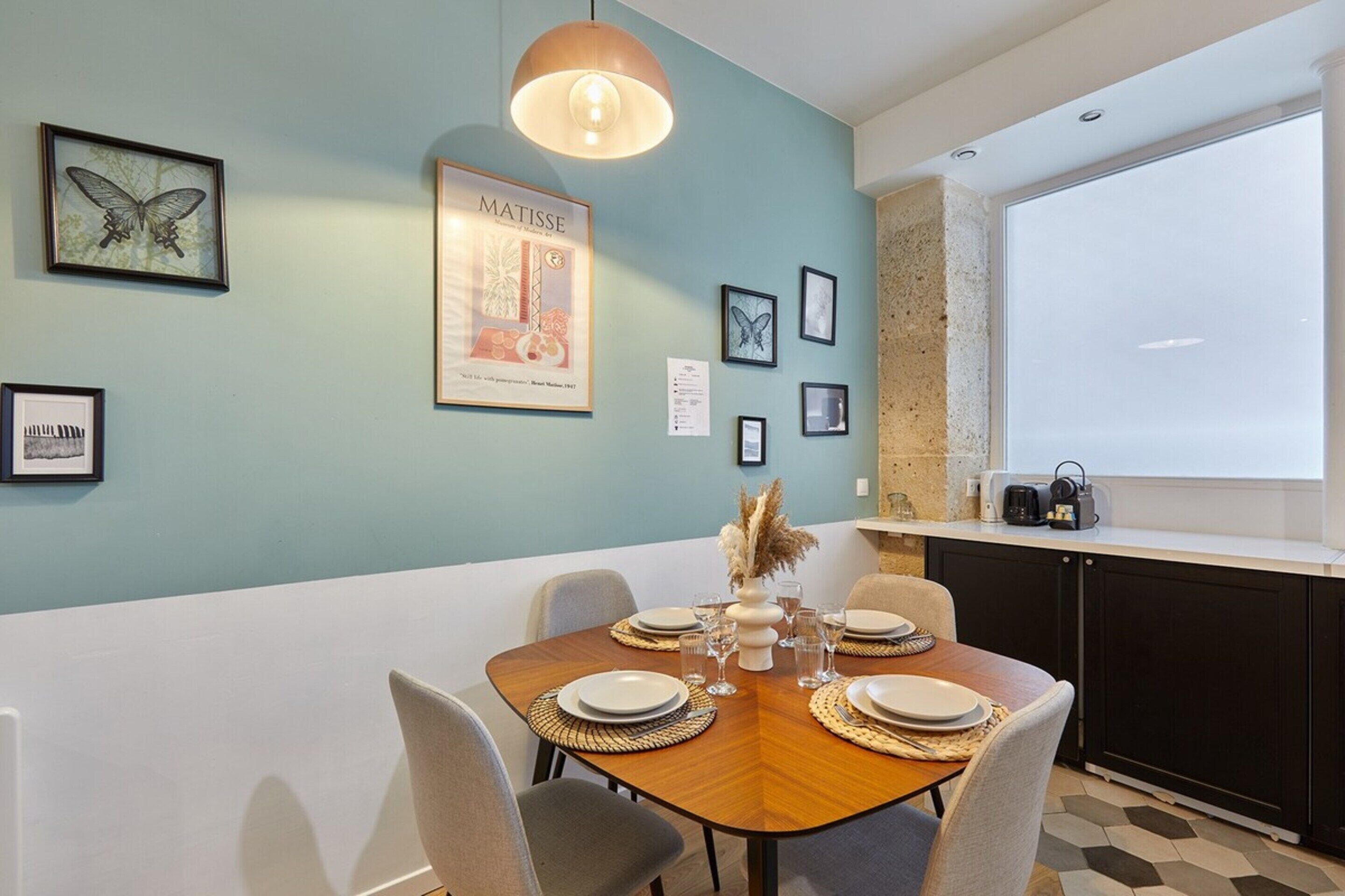 Een eethoek met een tafel voor vier personen, kunstwerken aan de wanden en een raam met uitzicht.