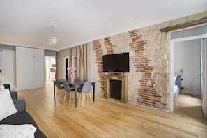 A modern living room with a fireplace, a dining area, and a TV mounted on a brick wall.