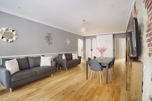 A modern living room with a grey sofa, a dining table with chairs, and a TV on a wooden cabinet.