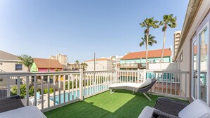 Un balcón con césped artificial, piscina y vistas de edificios circundantes.