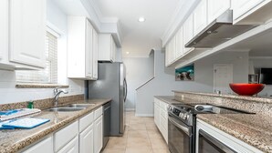 Una cocina moderna con armarios blancos, encimeras de granito, un refrigerador de acero inoxidable y un horno.
