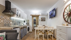 Una cocina compacta con comedor, un sofá y un televisor montado en la pared.
