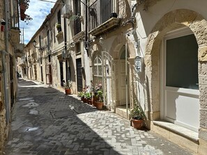 A narrow cobblestone street lined with historic buildings, potted plants, and a white door. - La casa di Rosa by Wonderful Italy (Siracusa)