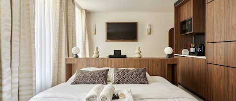 A hotel room with a large bed, wooden wardrobe, and a flat-screen TV on the wall.