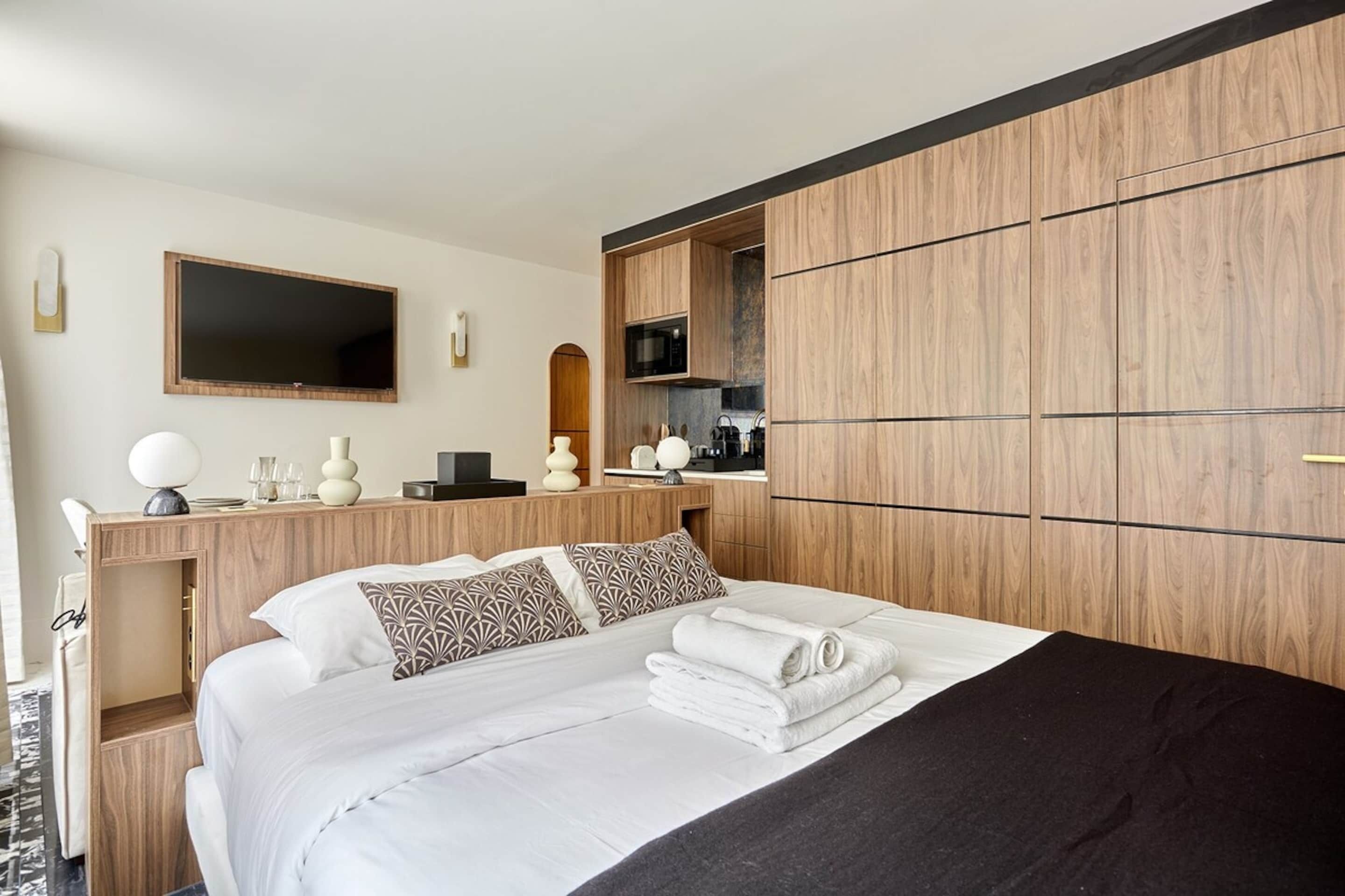 A hotel room with a bed, a desk with a flat-screen TV, a microwave, and a built-in wardrobe.