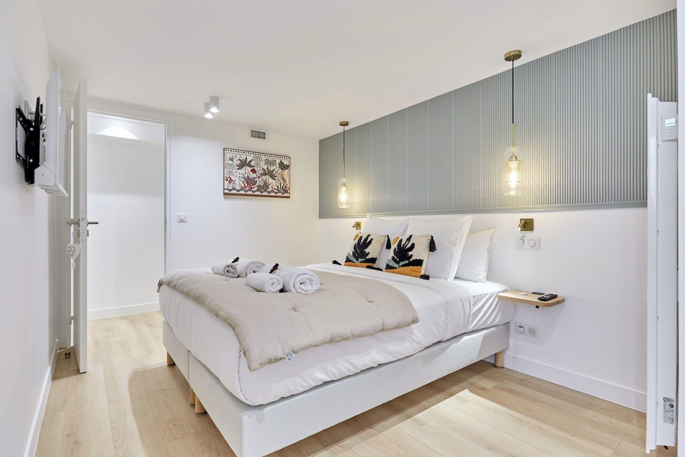 A modern bedroom with a large bed, a bedside table, a wall-mounted light fixture, and a door.