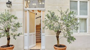 A building entrance with a wooden staircase, potted olive trees, and a white door. - Superb AC Apartment Paris Center Bourse Place (Paris)