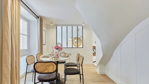 A dining area with a round table set for four, surrounded by wicker chairs, a large window with curtains, and a modern wall art piece. - Superb AC Apartment Paris Center Bourse Place (Paris)