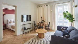 A modern living room with a sofa, a TV, a dining table with chairs, and a balcony with curtains. - Sublim & NEW Apartement St Germain/notre Dame (Paris)