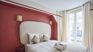 A hotel room with a large bed, two bedside lamps, a window with curtains, and a view of buildings outside. - Sublim & NEW Apartement St Germain/notre Dame (Paris)