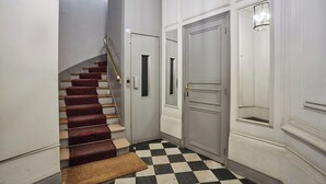A hallway with a checkered floor, a staircase with red carpeted steps, and a closed door with a small window. - Sublim & NEW Apartement St Germain/notre Dame (Paris)