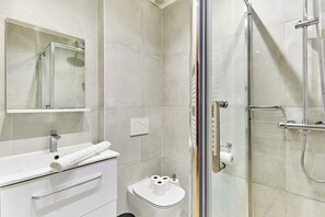 A modern bathroom with a glass-enclosed shower, a white sink with a towel, and a toilet with toilet paper.