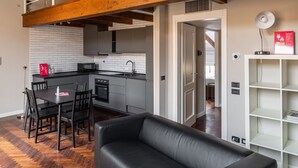 Una sala de estar moderna con un sofá de cuero negro, piso de madera y vigas de madera a la vista en el techo.