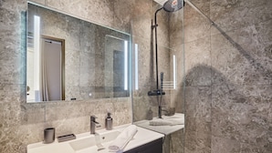 A modern bathroom with a large mirror, a sink, a shower, and marble walls.