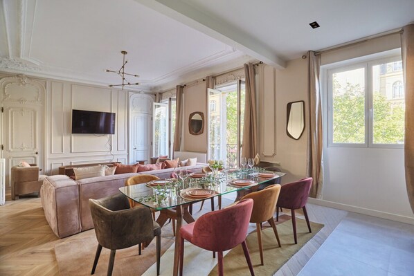 A dining area with a glass table, red chairs, and a sofa.