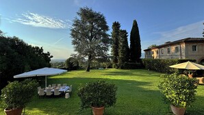 A well-maintained garden with a dining area, a large tree, and a building in the background. - VILLA PARADISO, stunning XVII century villa on the hills at 7 kms east of Lucca (Capannori)
