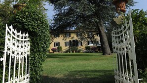 A large, yellow building with a symmetrical facade, surrounded by a well-maintained lawn and mature trees. - VILLA PARADISO, stunning XVII century villa on the hills at 7 kms east of Lucca (Capannori)