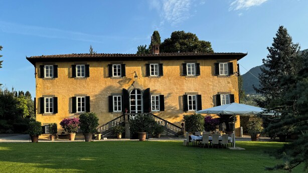 A large, yellow building with a staircase leading to a balcony, surrounded by a well-maintained lawn and potted plants. - VILLA PARADISO, stunning XVII century villa on the hills at 7 kms east of Lucca (Capannori)
