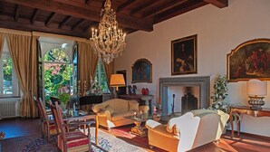 A spacious living room with a fireplace, a chandelier, and a large window with curtains. - VILLA PARADISO, stunning XVII century villa on the hills at 7 kms east of Lucca (Capannori)