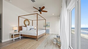 Une chambre à coucher avec un lit à baldaquin, un ventilateur de plafond, une grande fenêtre avec vue, une table de chevet avec une lampe et une commode.