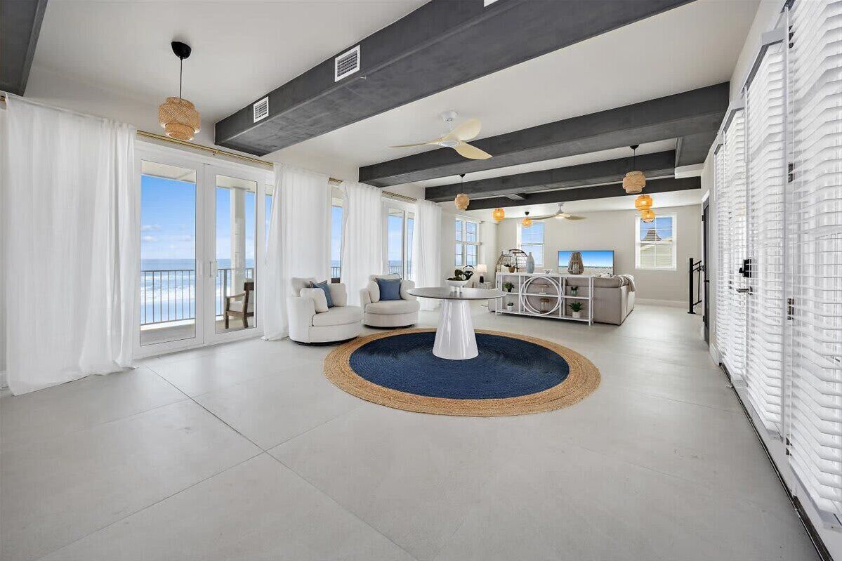 Un salón amplio con una mesa redonda grande, sofás blancos y vistas al mar.