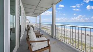 Un balcon abrité, doté de chaises blanches avec des coussins, offrant une vue sur la plage et s’ouvrant sur un ciel dégagé.