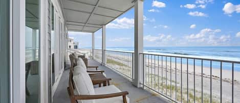 Un balcone coperto con sedie bianche imbottite, vista sulla spiaggia e cielo sereno.